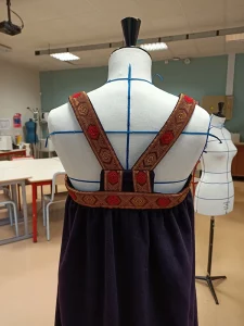 Photo des bretelles de dos d'une sarafane violette avec un galon doré et rouge sur un mannequin de couture, costume traditionnel russe